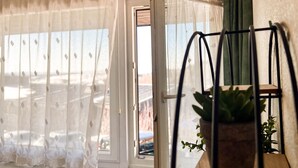 Una habitación con un ventanal cubierto por cortinas traslúcidas, una puerta que da al exterior y un macetero de metal con una planta en maceta.
