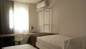 A hotel room with a bed, a desk, a chair, and a wardrobe.