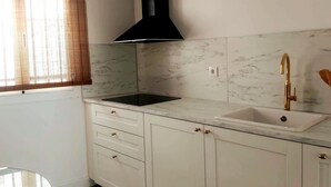 A kitchen with a black range hood, white cabinets, a marble backsplash, and a gold faucet.