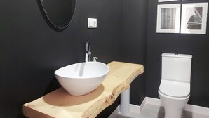 A modern bathroom with a white vessel sink on a wooden countertop, a toilet, and a wall-mounted mirror.