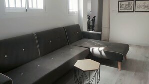 A modern living room with a dark grey sectional sofa, a hexagonal coffee table, and a dining area in the background.