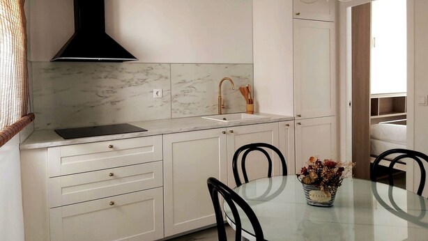 A modern kitchen with white cabinets, a black range hood, a marble backsplash, and a glass dining table with chairs.
