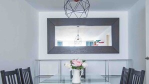 A modern dining area with a glass table surrounded by black chairs, a vase with flowers, and a geometric pendant light. - Comfortable apartment near Seville city center (Sevilla)