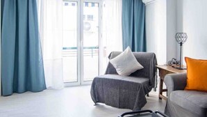 A modern living room with a grey armchair, a sofa with an orange cushion, and a small table with a lamp. - Comfortable apartment near Seville city center (Sevilla)