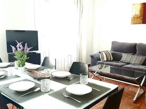 A dining area with a table set for four, a sofa, and a television in the background. - Unforgettable stay in Seville at Gravina 54 (Sevilla)