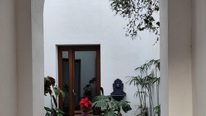 A small outdoor patio with a wooden table and chairs, surrounded by potted plants and a decorative wall-mounted sculpture.