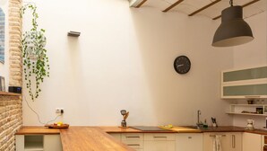 A kitchen with a wooden table, bar stools, a hanging plant, a clock, and a hanging light fixture.