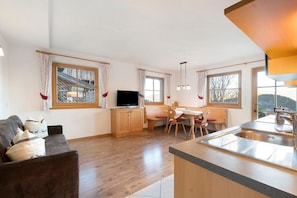 Una cocina moderna con armarios de madera, una zona de comedor con mesa y sillas, y un sofá con cojines decorativos.