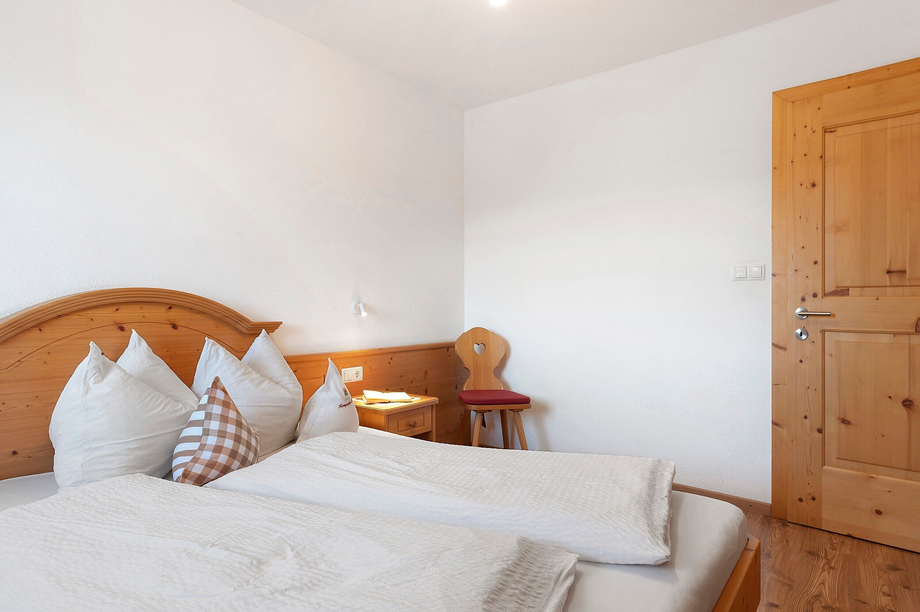Une chambre à coucher avec une tête de lit en bois, une porte en bois, une petite table de chevet et une chaise avec un coussin rouge.