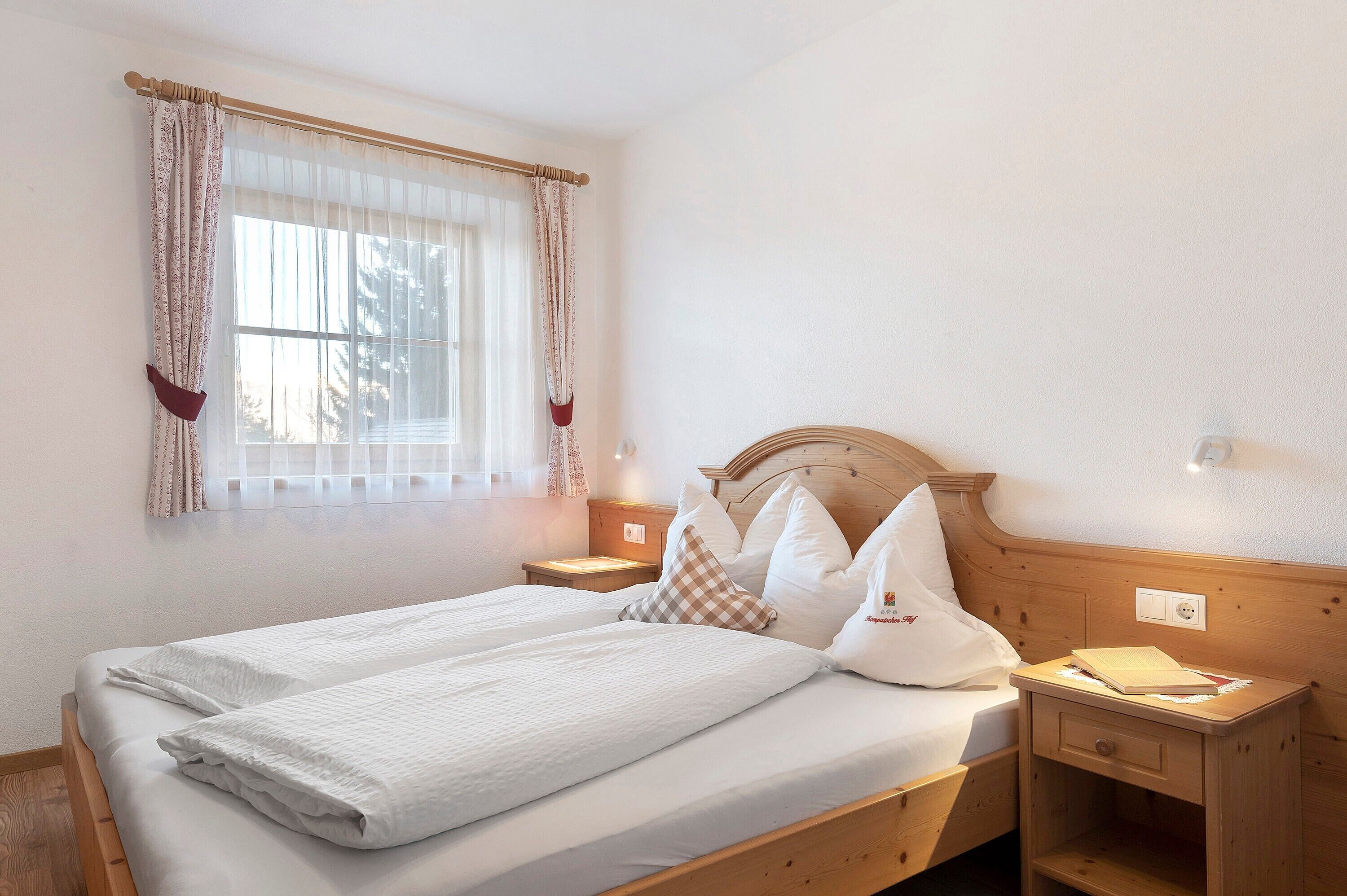 A double bed with white linens, a wooden headboard, and a bedside table with a lamp.