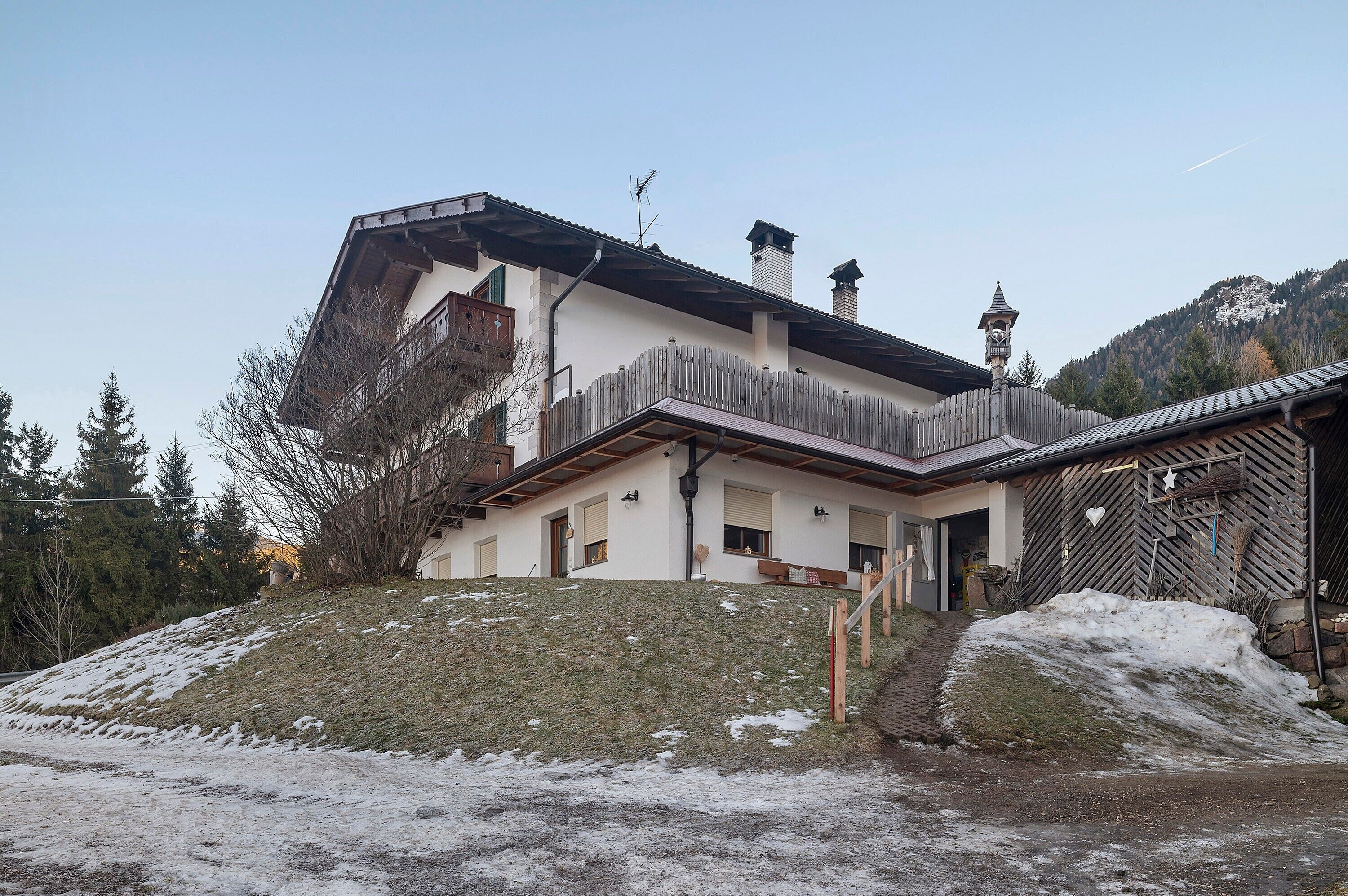 Ein zweistöckiges Haus mit geneigtem Dach, einem Holzzaun und einem kleinen Glockenturm.