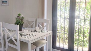 Ein Essbereich mit einem weißen Tisch, gedeckt für vier Personen, einer Zimmerpflanze und einem Fenster mit Metallgitter.