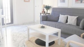 Ein Wohnzimmer mit grauem Sofa, einem weißen Couchtisch und einem kleinen Beistelltisch mit Lampe und Vase.