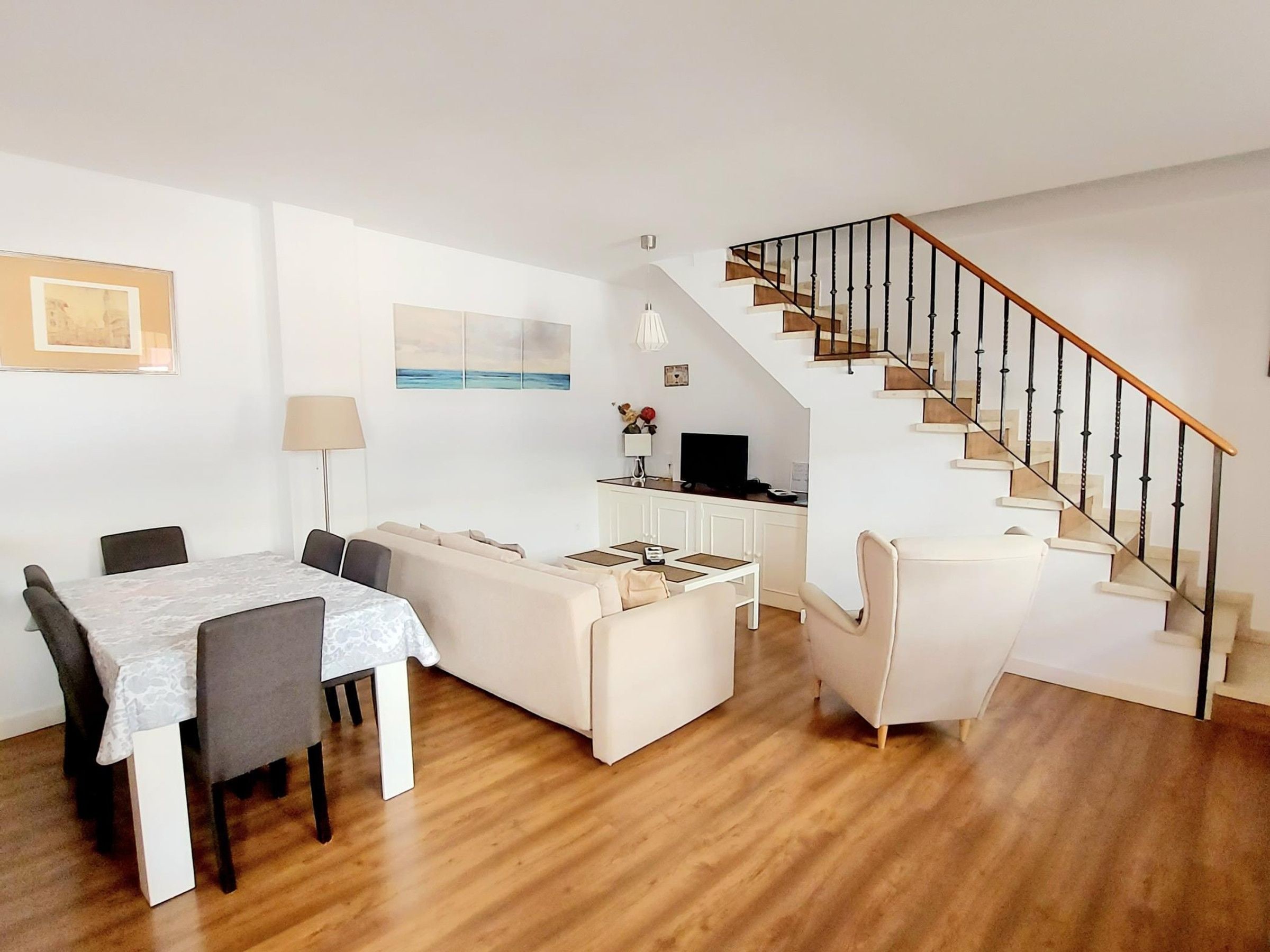 Ein modernes Wohnzimmer mit Essbereich, einer Treppe und einer Küche im Hintergrund.