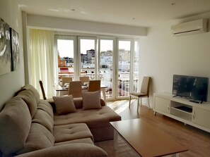 A modern living room with a large sofa, a TV, and a balcony with city views. - Bright Apartment in Triana, Seville (Sevilla)