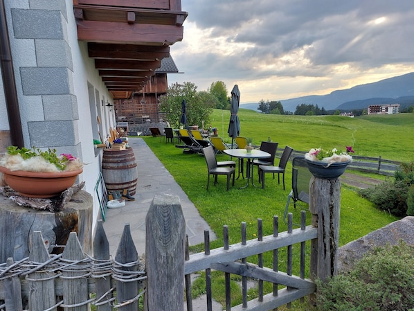 A patio with outdoor seating, a wooden fence, and a view of a green field and mountains.