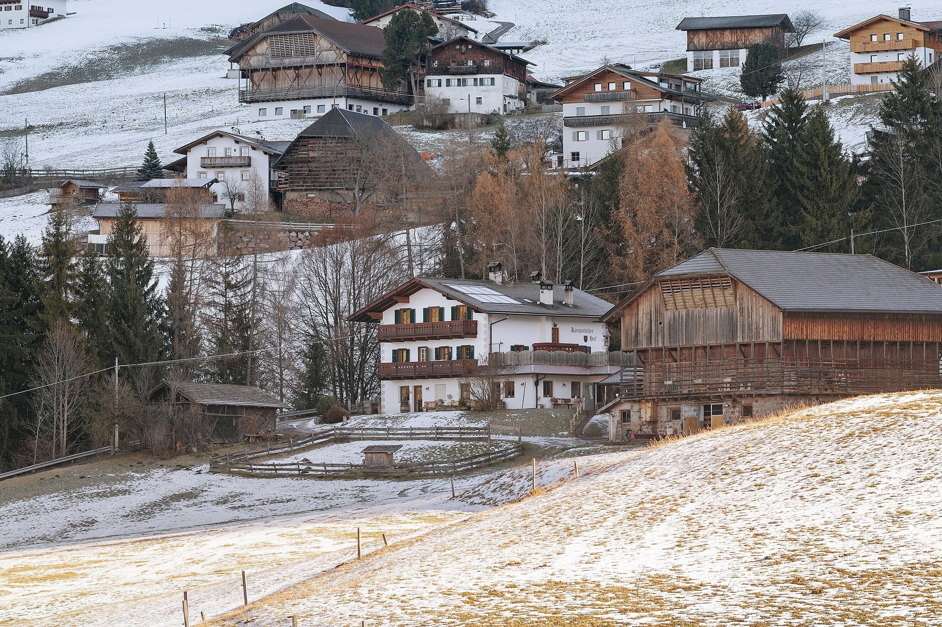 A cluster of traditional wooden buildings with balconies, situated on a hillside with snow-covered ground.