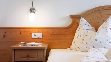 Una mesita de noche de madera con una lámpara, una cama con ropa de cama estampada con motivos florales y un enchufe de pared.