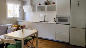 Une cuisine de taille réduite avec des meubles blancs, un four encastré et un réfrigérateur.