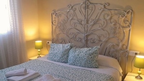 Un lit bien fait, avec une couvre-lit à motifs, deux oreillers et des serviettes pliées posées sur une tête de lit ornée d’un motif décoratif.