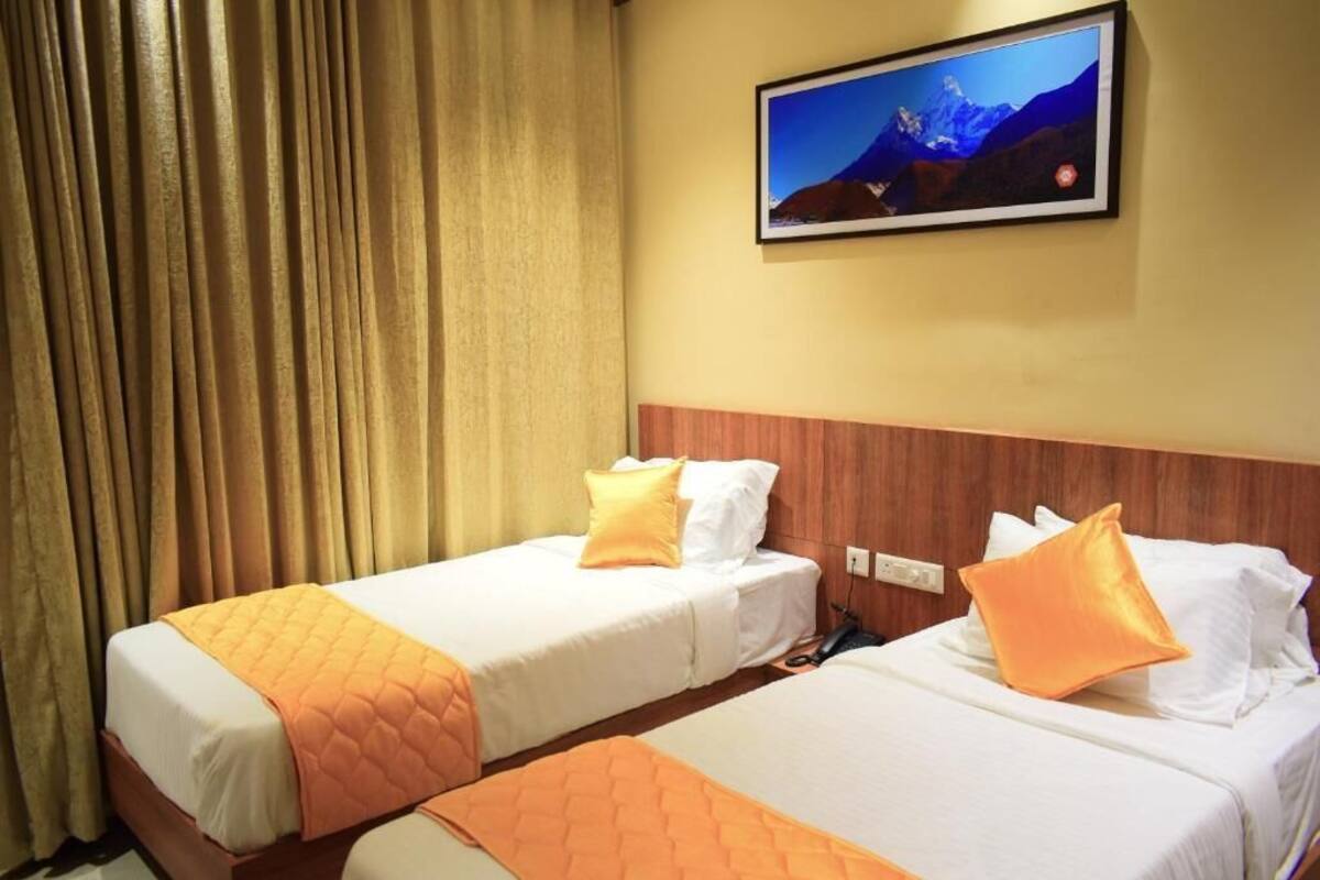 Een hotelkamer met twee bedden, elk voorzien van witte beddengoed en oranje accenten. Boven de bedden hangt een schilderij aan de muur.