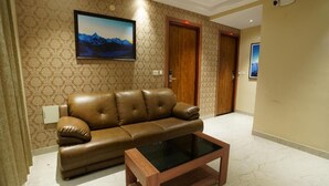A living room with a brown leather sofa, a glass coffee table, and patterned wallpaper. - Hotel Valley Vista (Visakhapatnam)