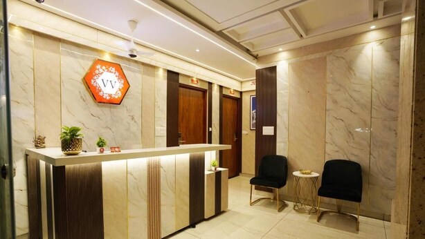 A reception area with a marble reception desk, two black chairs, and a hexagonal sign with 'VV' on it. - Hotel Valley Vista (Visakhapatnam)