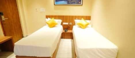 A hotel room with two single beds, wooden headboards, white bedding, and a framed picture on the wall.