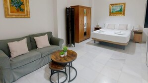A modern hotel room with a sofa, a bed, a round table with plants, and two paintings on the walls.