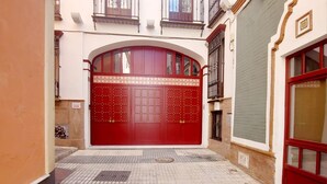 A red gate with decorative metalwork, a tiled pavement, and a building with a balcony.