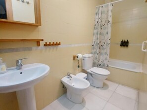A bathroom with a sink, two toilets, a bidet, a shower curtain, and toiletries on the wall. - Peaceful studio for couples in Seville center (Sevilla)