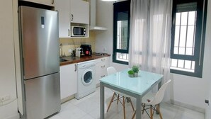 A compact kitchen with a refrigerator, microwave, washing machine, and a dining table with chairs.