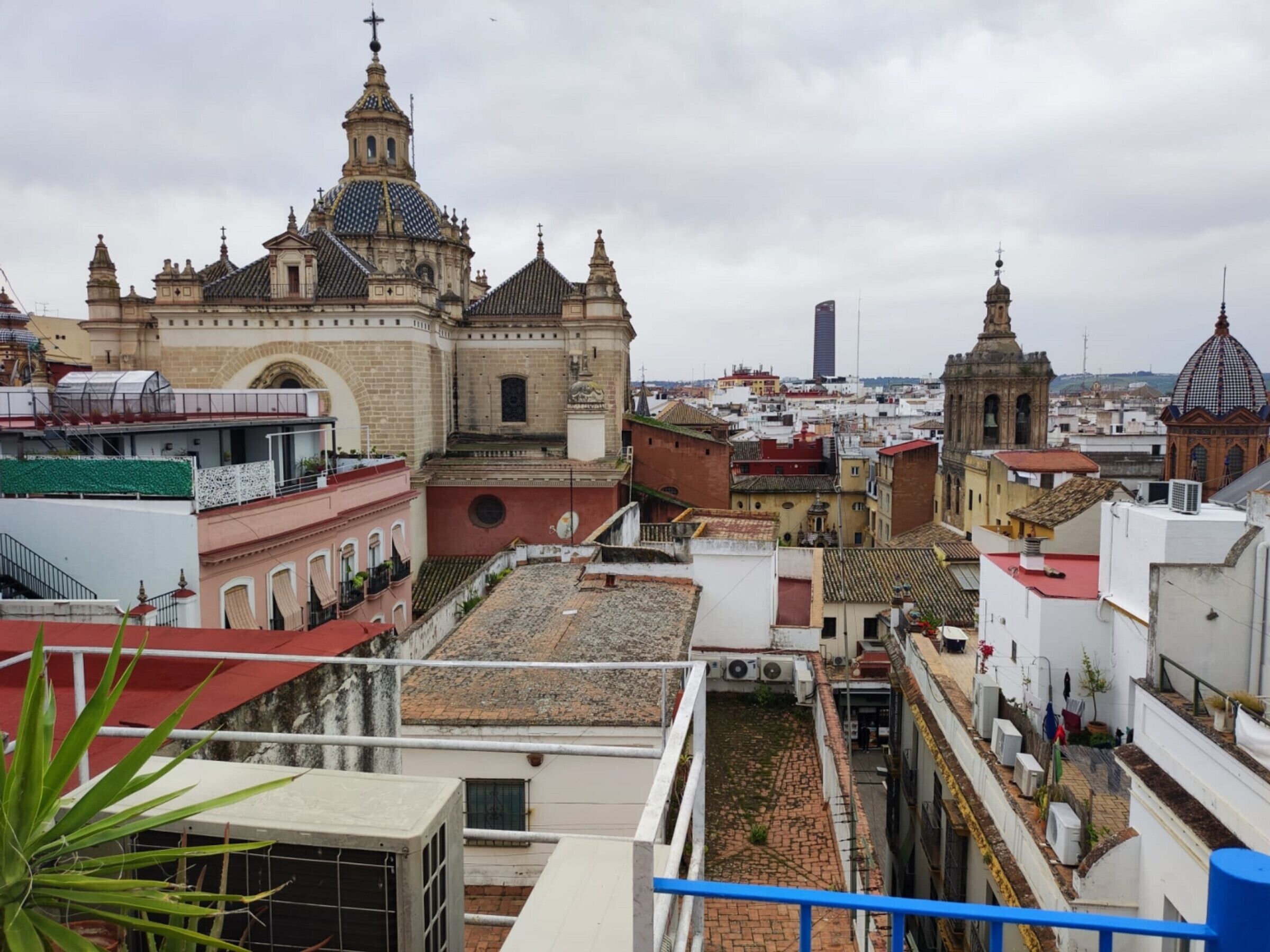 Un edificio histórico con una cúpula destacada y un campanario, rodeado de construcciones modernas y un cielo despejado.