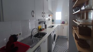 A modern kitchen with white cabinets, a built-in washing machine, and a red cutting board. - Duplex with Private Terrace in Seville Center (Sevilla)