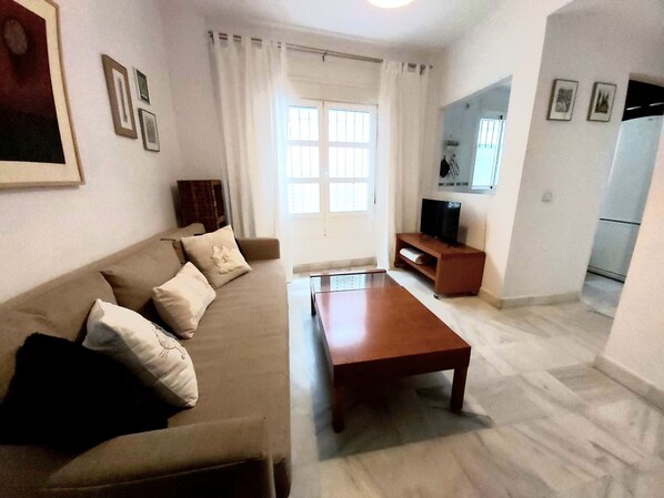 A living room with a sofa, coffee table, TV stand, and a window with curtains.