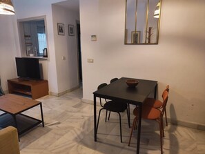 Un salon moderne avec un téléviseur, une table à manger avec des chaises et un grand miroir au mur.