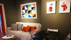 Ein modernes Wohnzimmer mit einer Couch, zwei Sesseln, einem kleinen Tisch und Kunstwerken an der Wand.