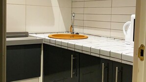 Eine Küche mit weiß gefliestem Spritzschutz, einem Waschbecken mit orangefarbenem Becken und einem Wasserkocher auf der Arbeitsfläche.