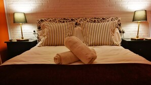 Ein ordentlich bezogenes Bett mit gestreifter Bettwäsche und einem zusammengerollten Handtuch, begleitet von zwei Nachttischlampen auf passenden Nachttischen.