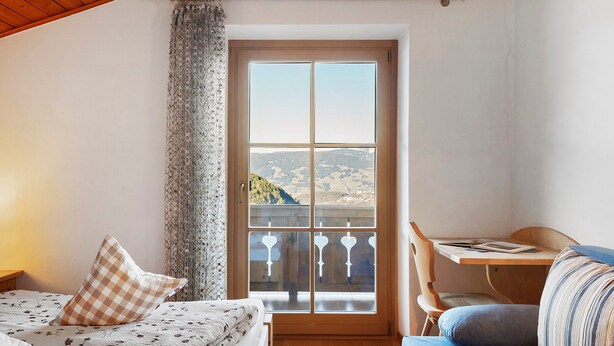 A room with a bed, a desk, and a view of a landscape through a window.