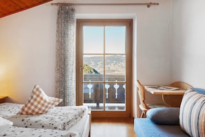 A room with a bed, a desk, and a view of a landscape through a window.