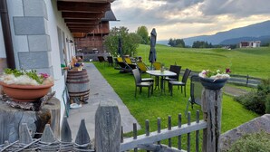 A patio with outdoor seating, a wooden fence, and a view of a green field and mountains.