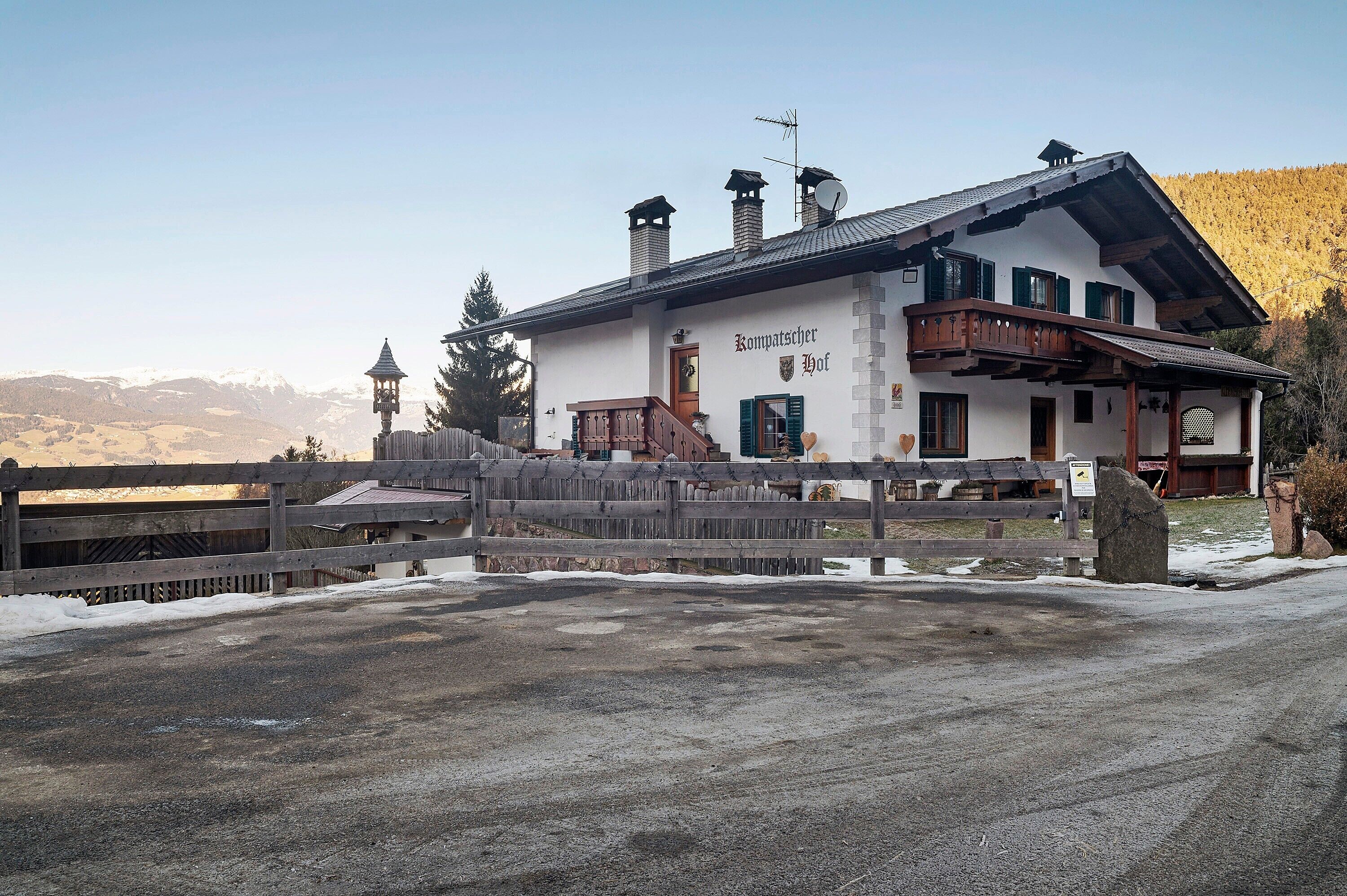 Een traditioneel gebouw in Alpenstijl met een houten balkon, een bord met de tekst 'Komptschehof' en een uitzicht op besneeuwde heuvels.