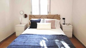 A bedroom with a bed, two bedside tables, a nightstand, a window with blinds, and a wall-mounted mirror. - Accessible house in Triana with private patio (Sevilla)