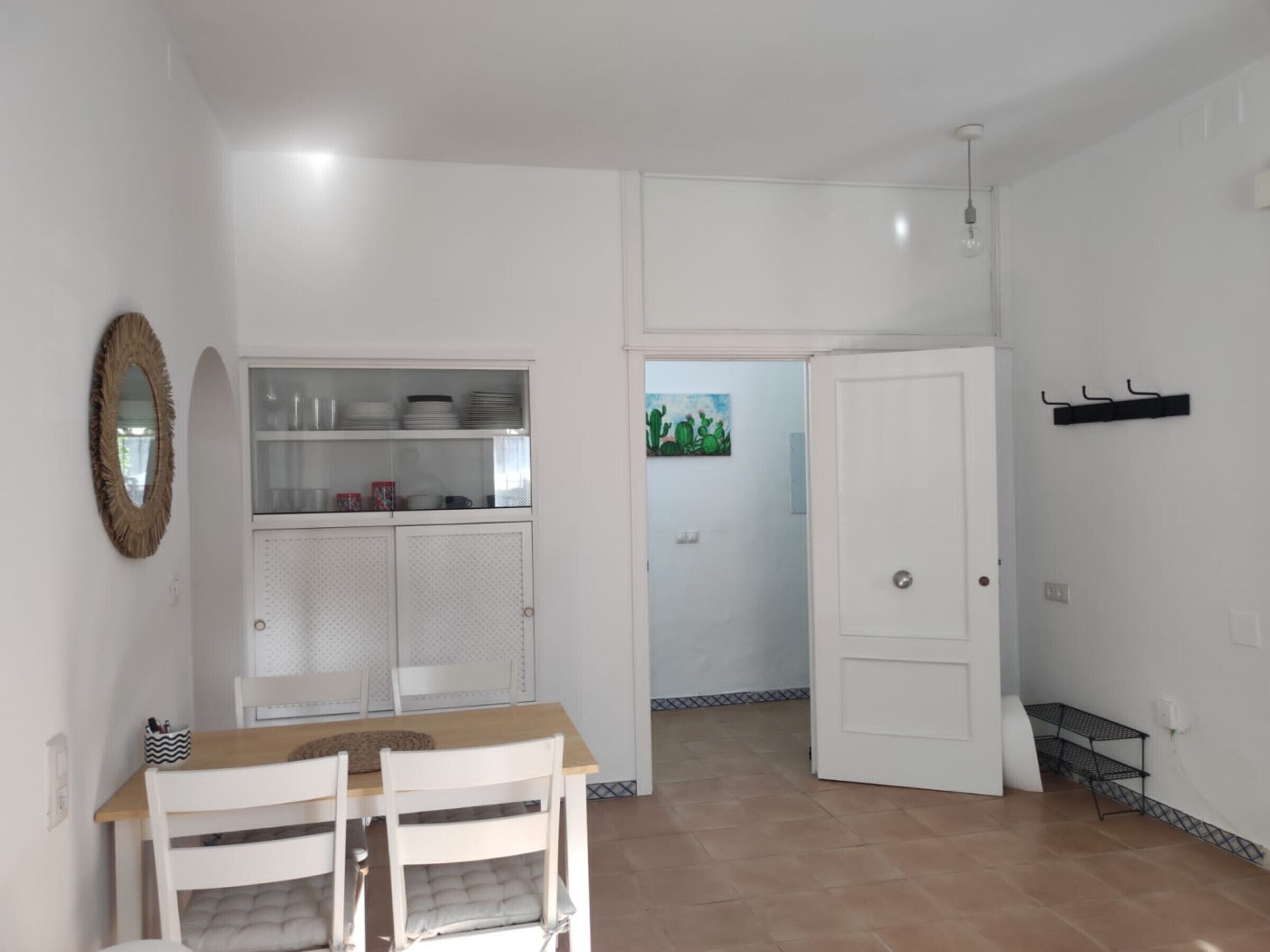 Uma sala de jantar com uma mesa e cadeiras, um armário com louças, uma porta e uma prateleira fixada na parede.