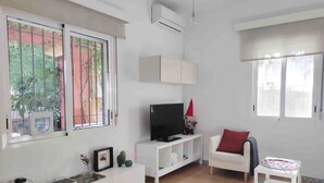 A living room with a TV, white furniture, a red cushion, and a small table with a tray. - Accessible house in Triana with private patio (Sevilla)