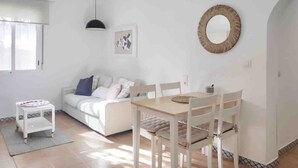 A bright living room with a white sofa, a small white table, and a wooden dining table with chairs. - Accessible house in Triana with private patio (Sevilla)