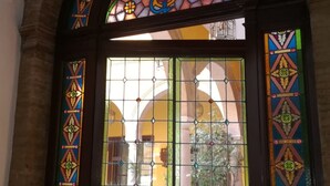 Een glas-in-loodraam met geometrische patronen en uitzicht op een gebouw met bogen.