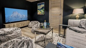 A modern living room with a large flat-screen TV, comfortable seating, a wooden ceiling, and a door with a wooden frame. - Chalet D'Espoir - Pure Alpine Luxury! (Montriond)