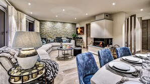 A modern living room with a stone wall, a fireplace, and a dining area set for a meal. - Chalet D'Espoir - Pure Alpine Luxury! (Montriond)